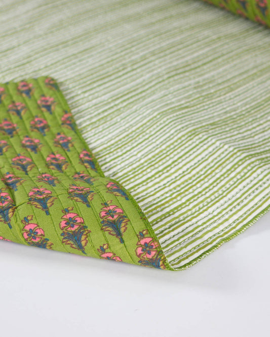 A close-up of a quilted cotton fabric showing two sides: one side is light green and white striped, and the other side is olive green with a pink and blue floral quilted pattern.