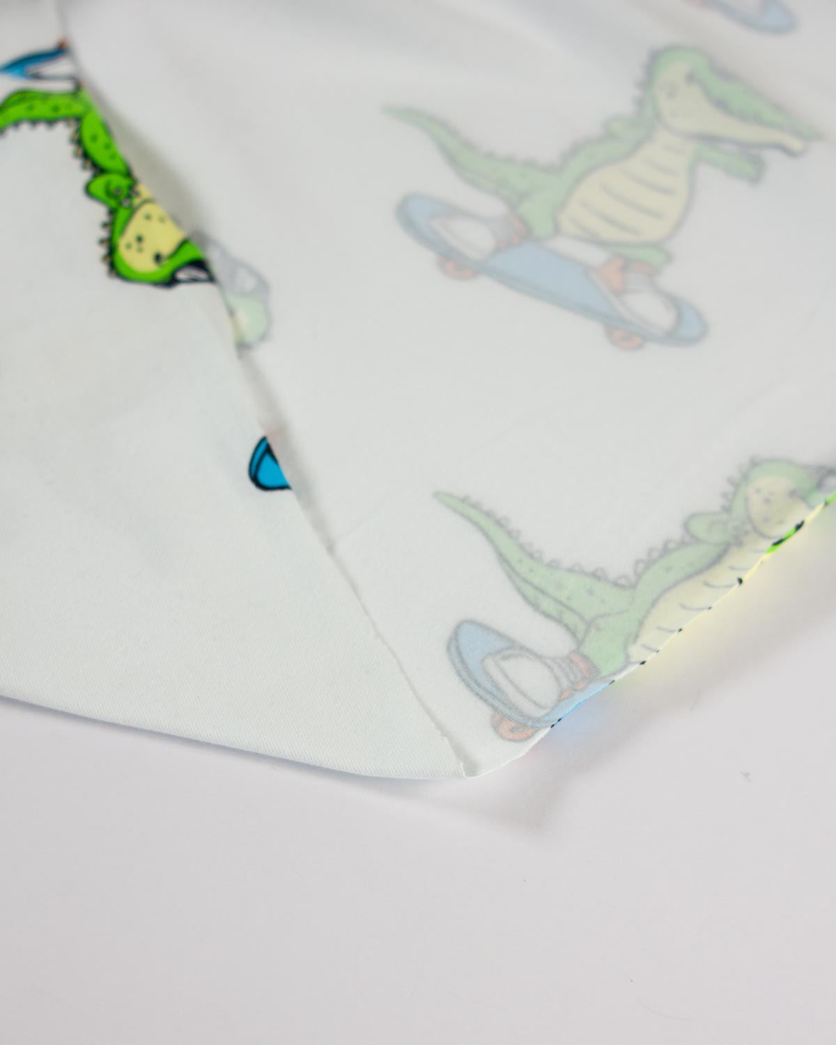 A close-up of a white jersey fabric featuring a playful print of cartoon alligators riding light blue skateboards.