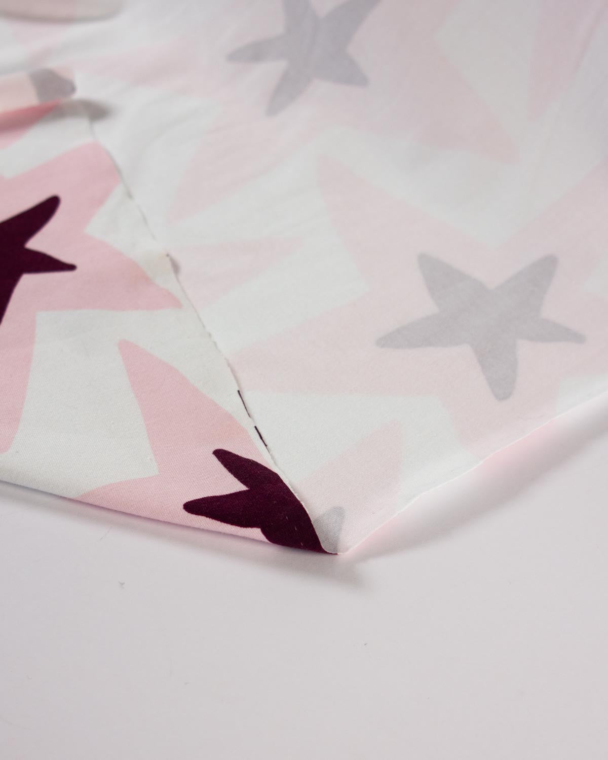 A close-up of a white fabric featuring a pattern of pink, white, and dark burgundy stars.