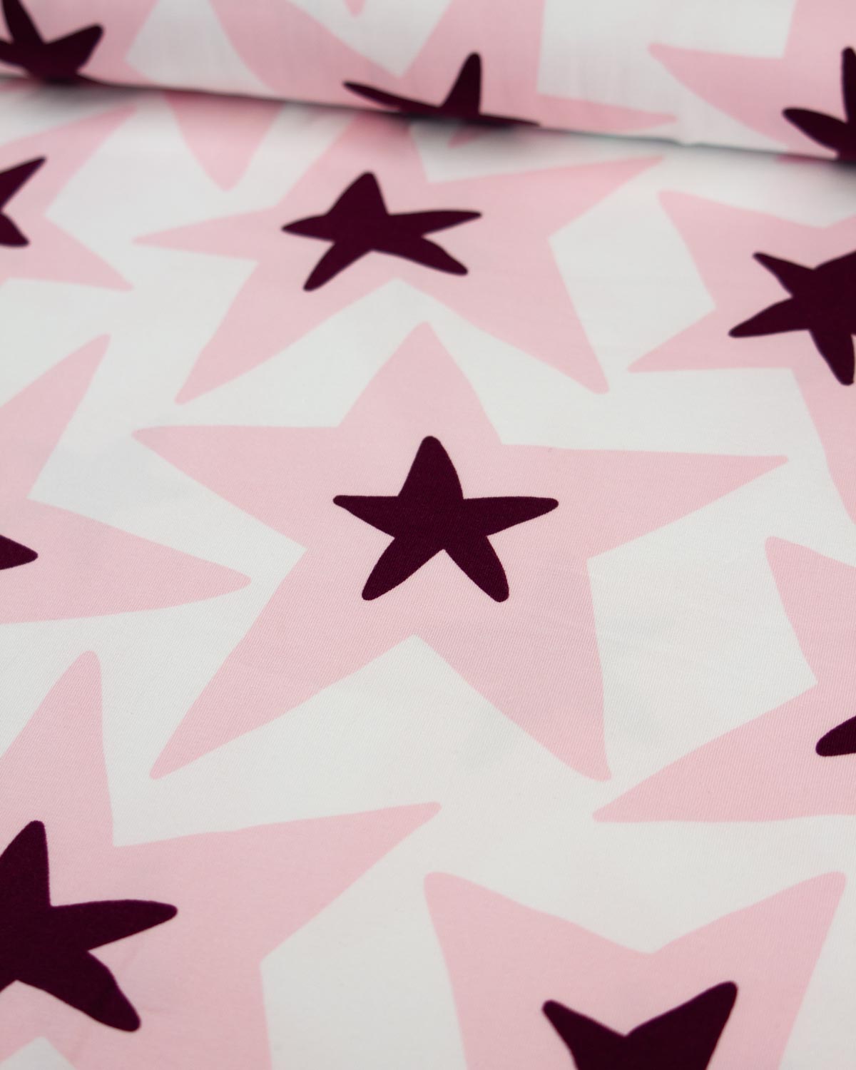 A close-up of a cotton jersey fabric pattern featuring large light pink stars with dark plum-purple five-pointed stars in the center, set against a white background.