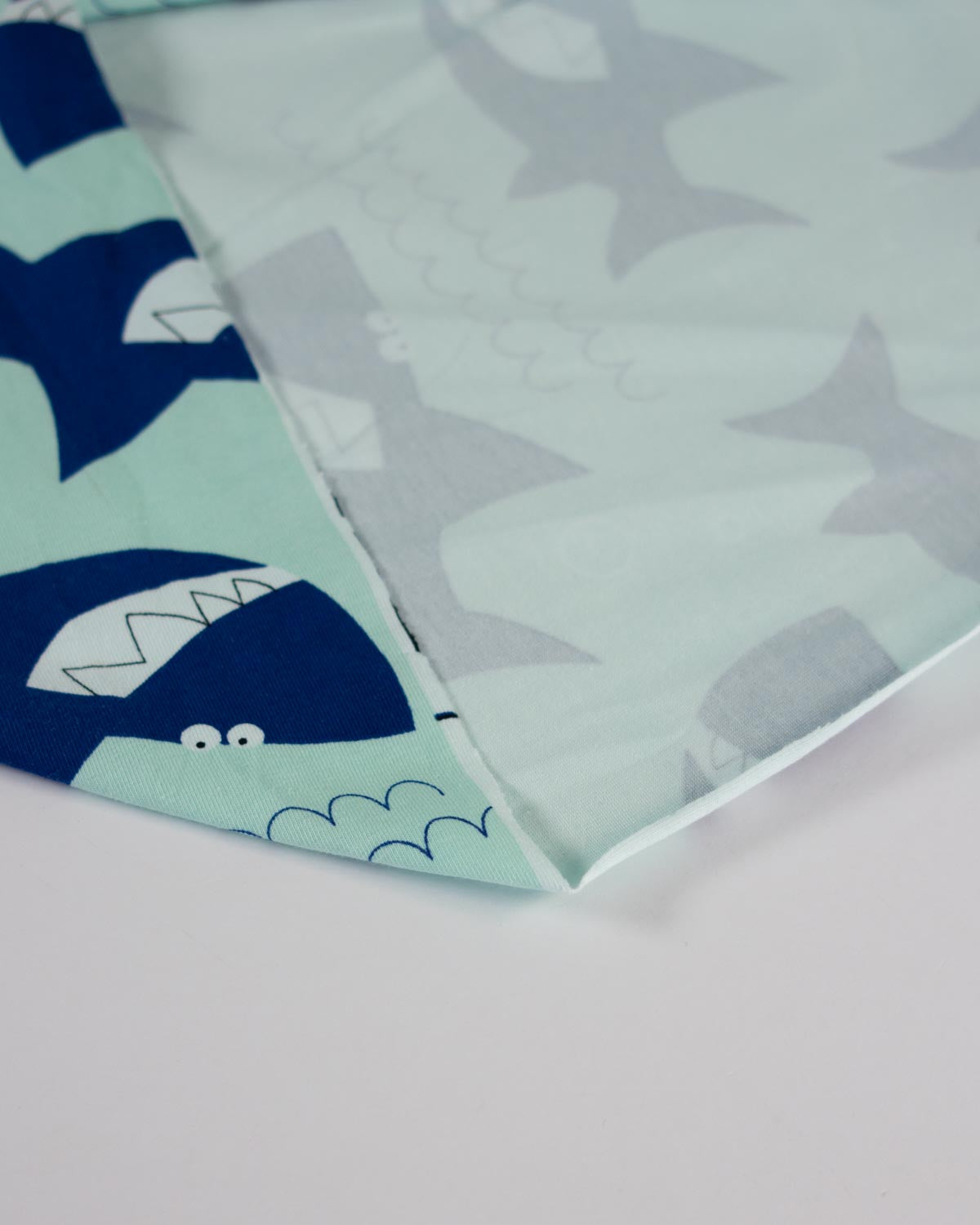 A close-up of a folded cotton jersey  fabric featuring an underwater shark pattern in navy blue, mint green, and light gray on a white background.