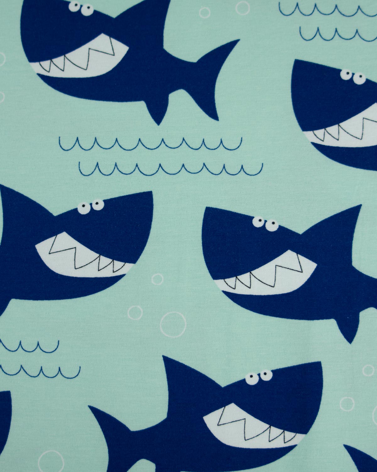 A close-up of a cotton jersey  fabric pattern featuring cartoonish dark blue sharks swimming on a light mint green background, with simple blue wave and bubble details.