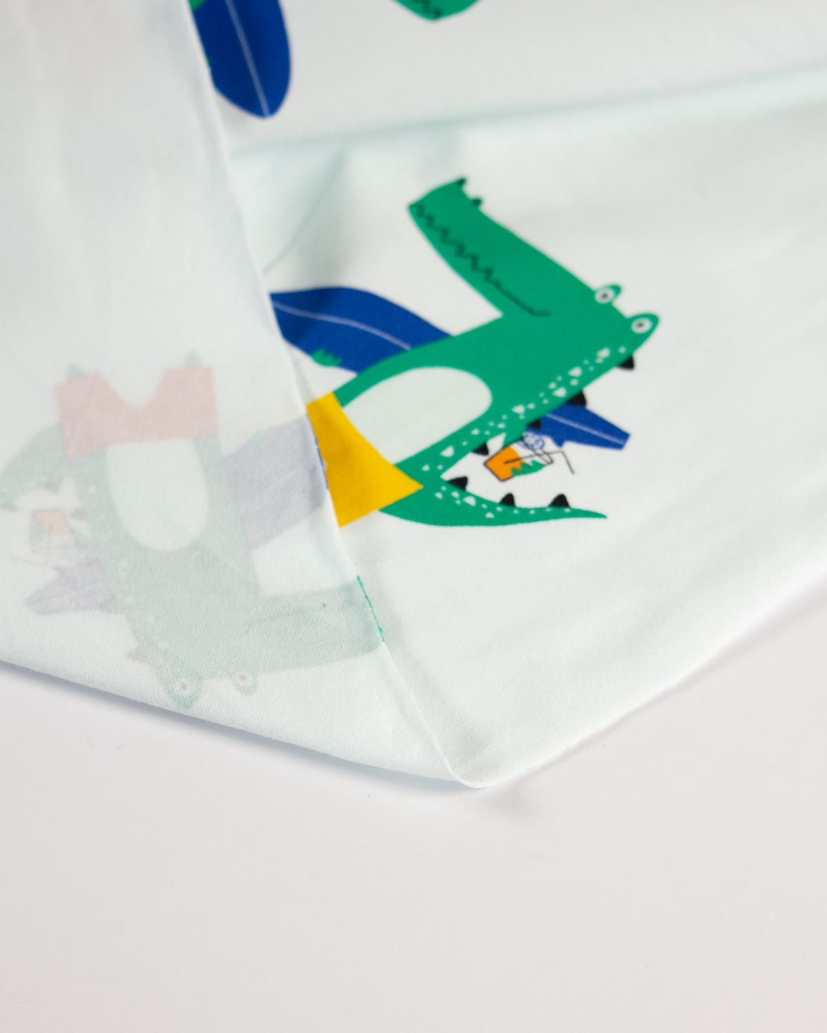 A close-up of a white cotton jersey fabric featuring a colorful cartoon crocodile print with green, blue, yellow, and pink details.