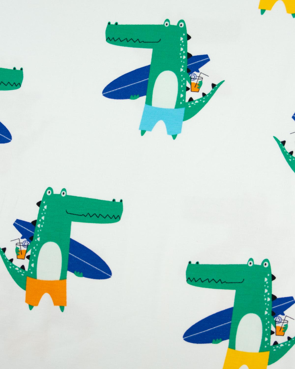 A close-up of a cotton jersey fabric pattern featuring green cartoon crocodiles wearing colorful swim trunks, with blue surfboards and beach umbrellas on a white background.