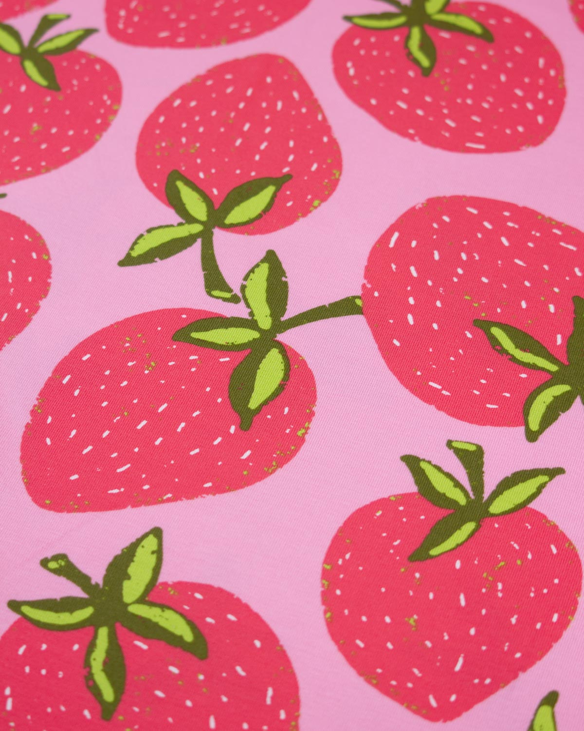 A close-up of a pink cotton jersey fabric pattern featuring illustrated red strawberries with green leaves and small white seed details.