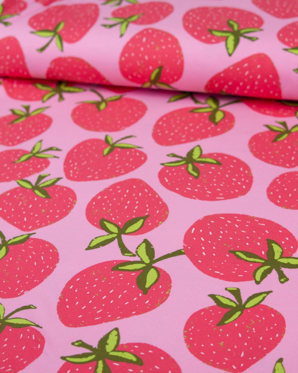 Pink cotton jersey fabric with a repeating strawberry print, featuring red strawberries with green leaves and stems.