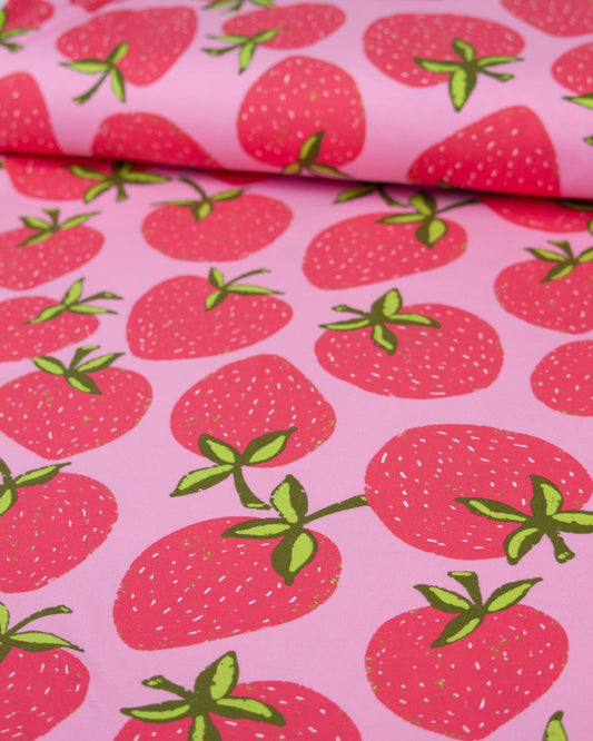 Pink cotton jersey fabric with a repeating strawberry print, featuring red strawberries with green leaves and stems.
