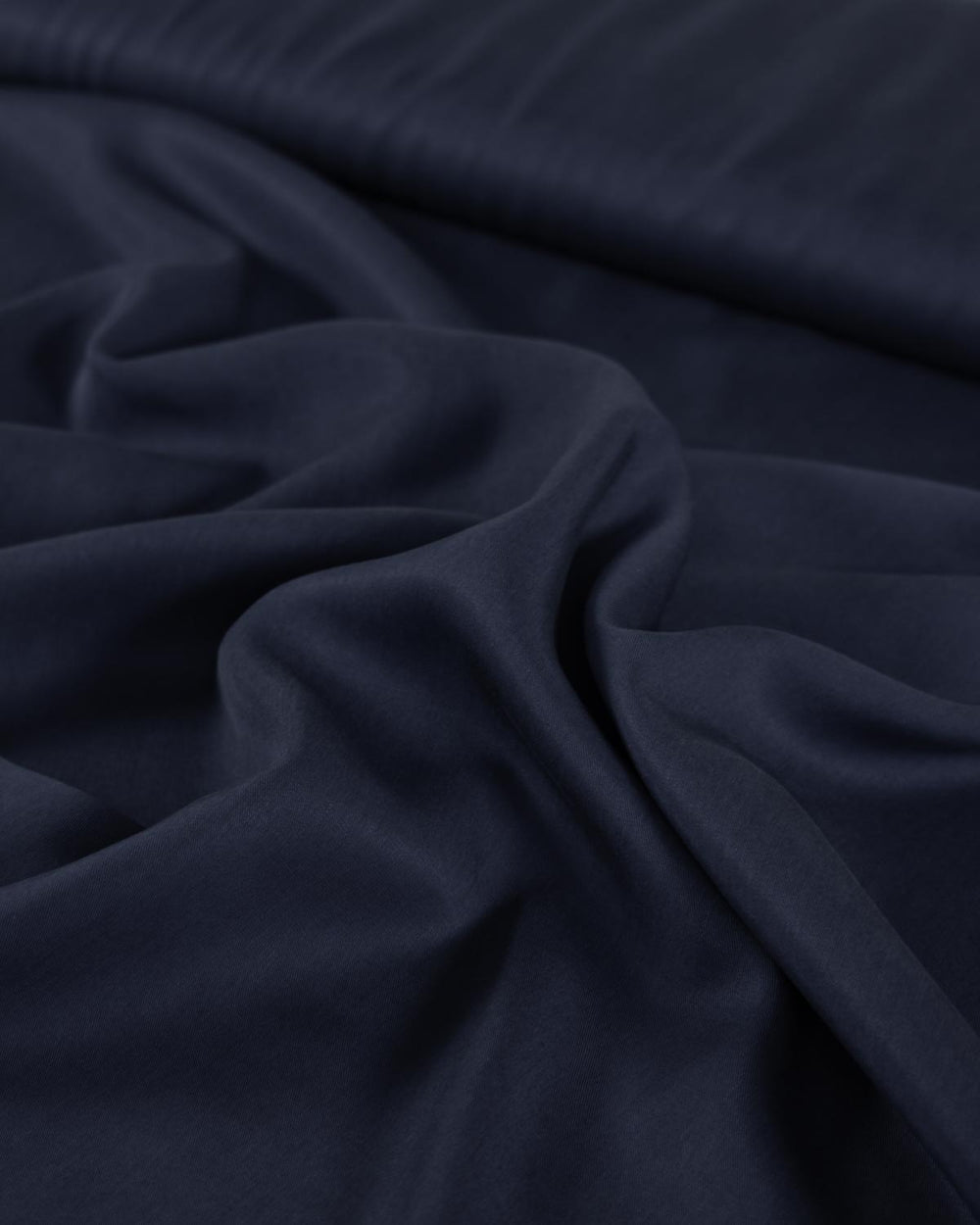 A close-up of dark navy blue tencel twill fabric with soft folds and a smooth texture.