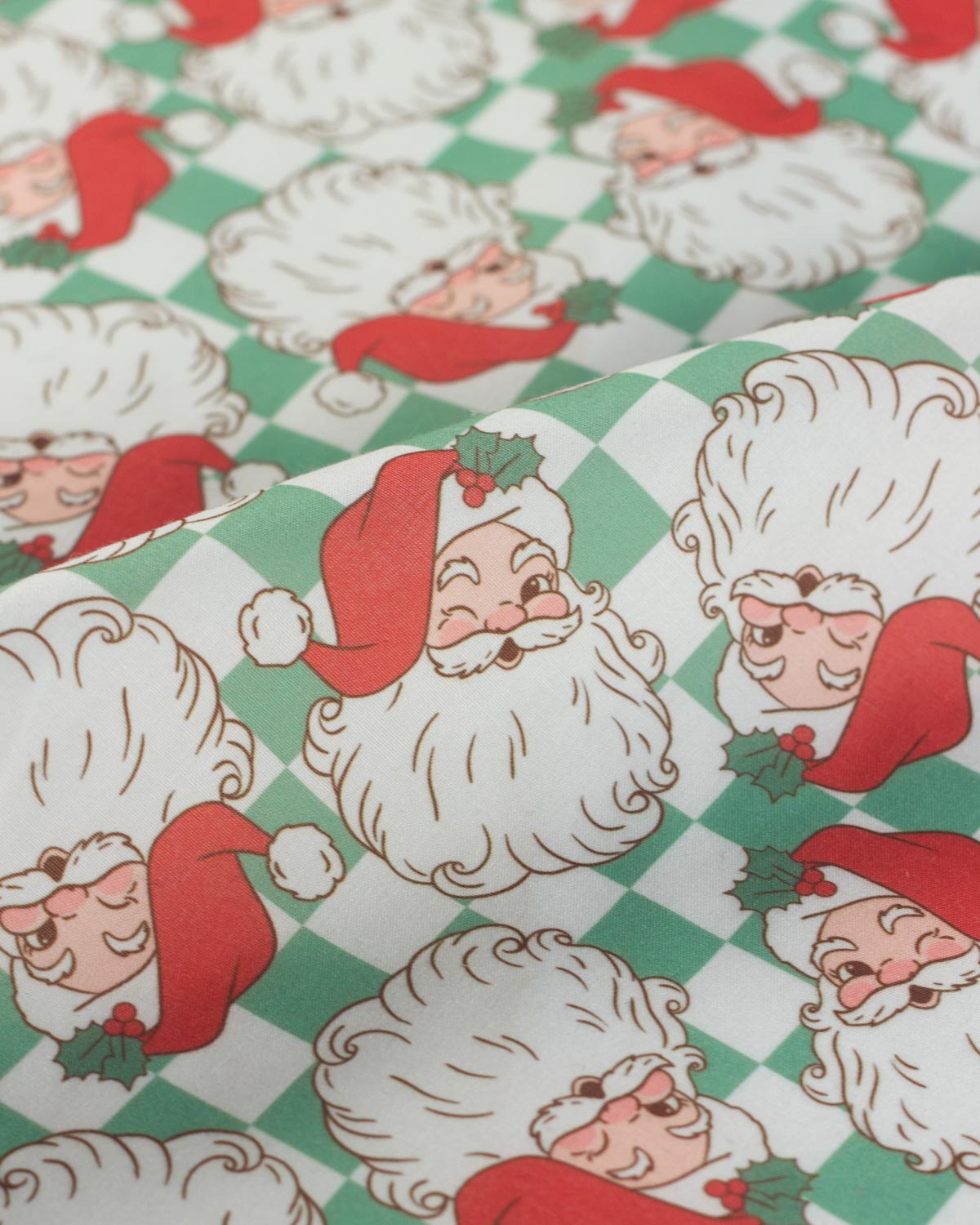 A close-up of a Christmas-themed fabric featuring a repeating pattern of Santa Claus faces on a green and white checkered background.