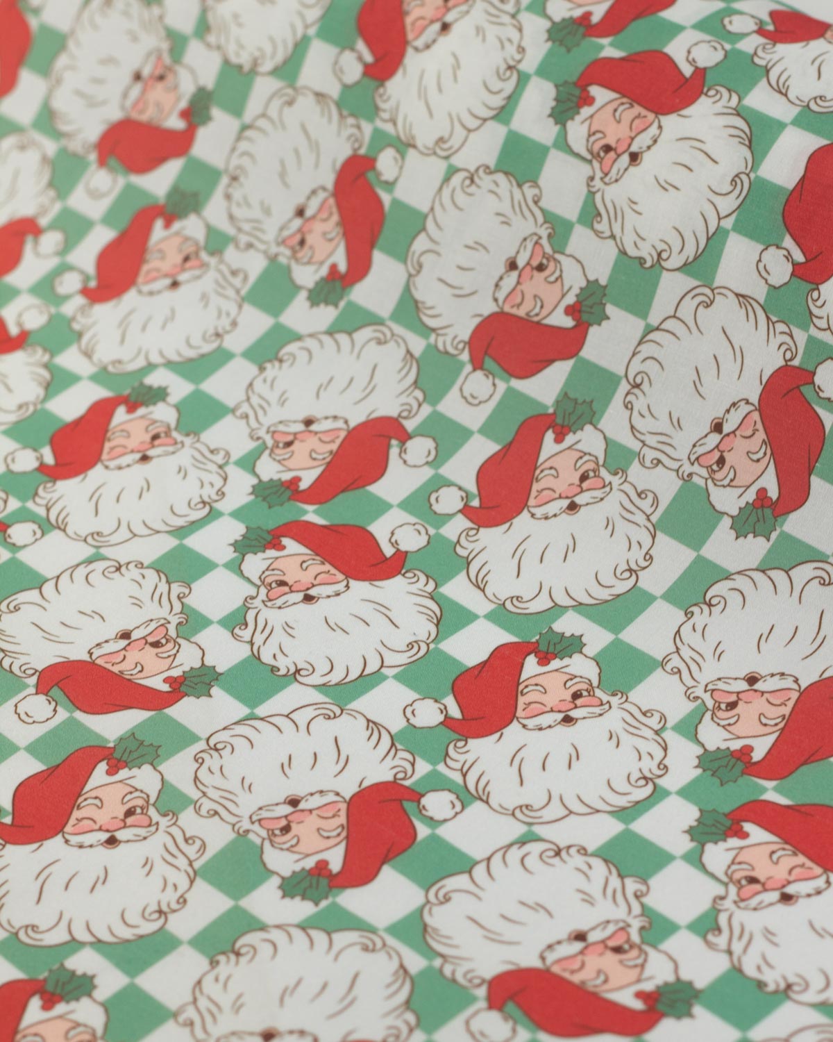 A close-up of a polycotton fabric with repeating Christmas pattern featuring Santa Claus faces on a green and white checkered background.
