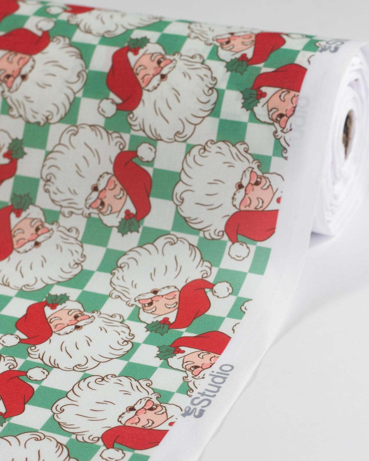 A roll of Christmas polycotton fabric featuring a repeating pattern of Santa Claus faces on a green and white checkered background.