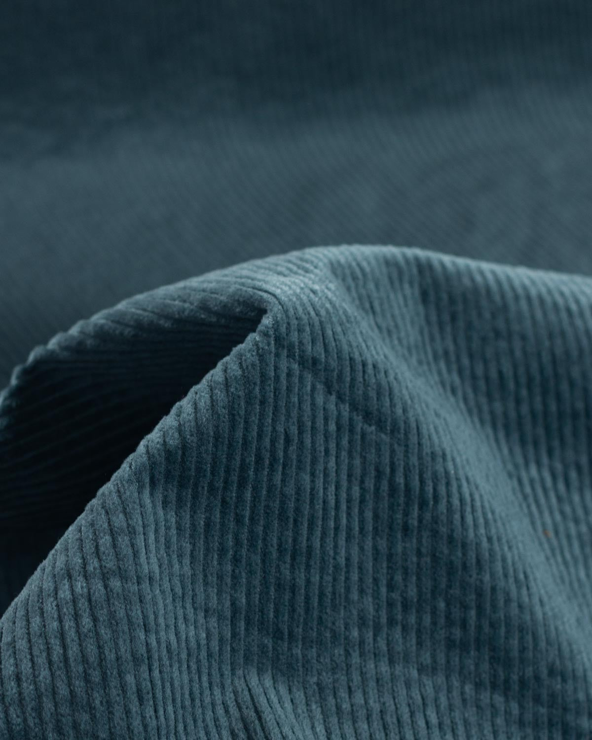 Close-up of a dark teal cotton corduroy fabric with a ribbed texture and soft folds.