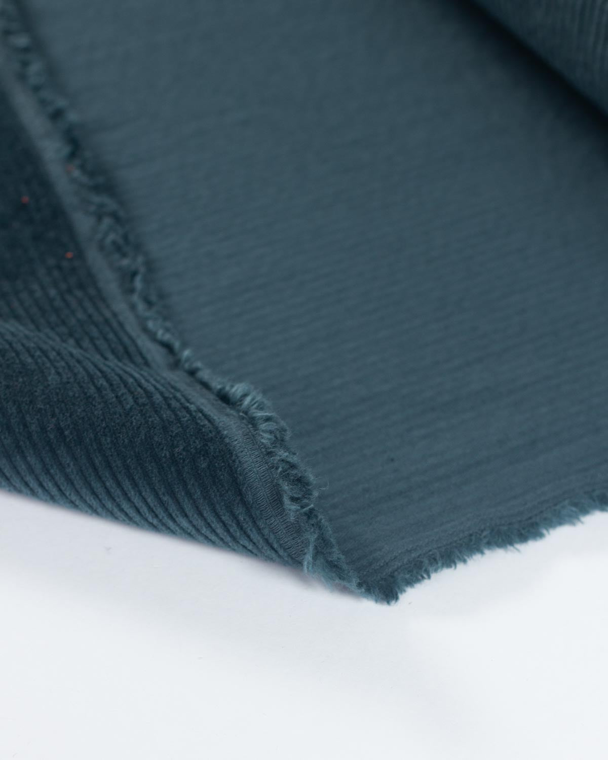 A close-up of a dark teal corduroy fabric folded over to show its texture and colour against a plain white background.