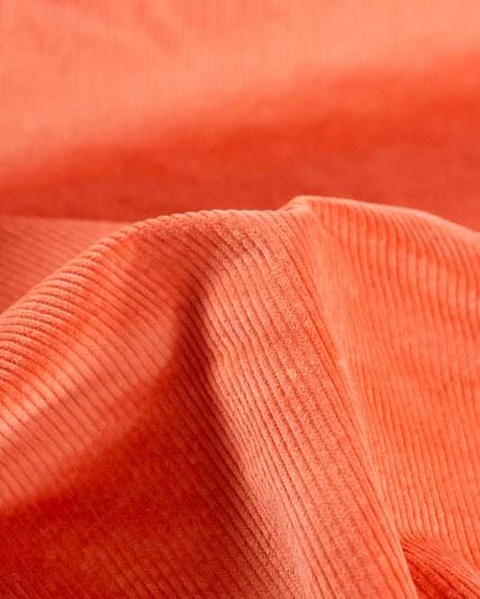 A close-up of draped orange cotton corduroy fabric showing its ribbed texture and soft folds.