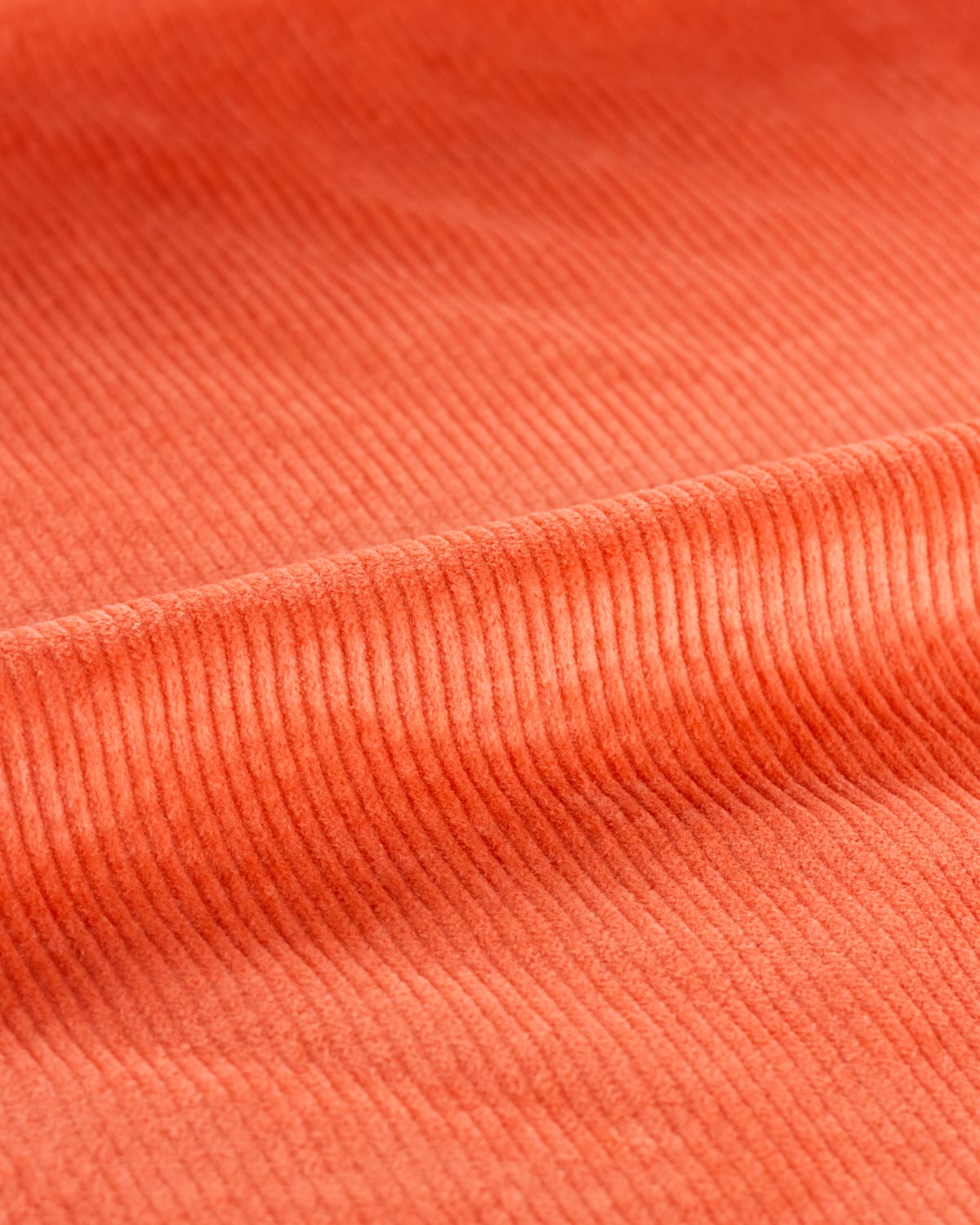 A close-up of textured orange cotton corduroy fabric with a diagonal ribbed pattern and soft folds.