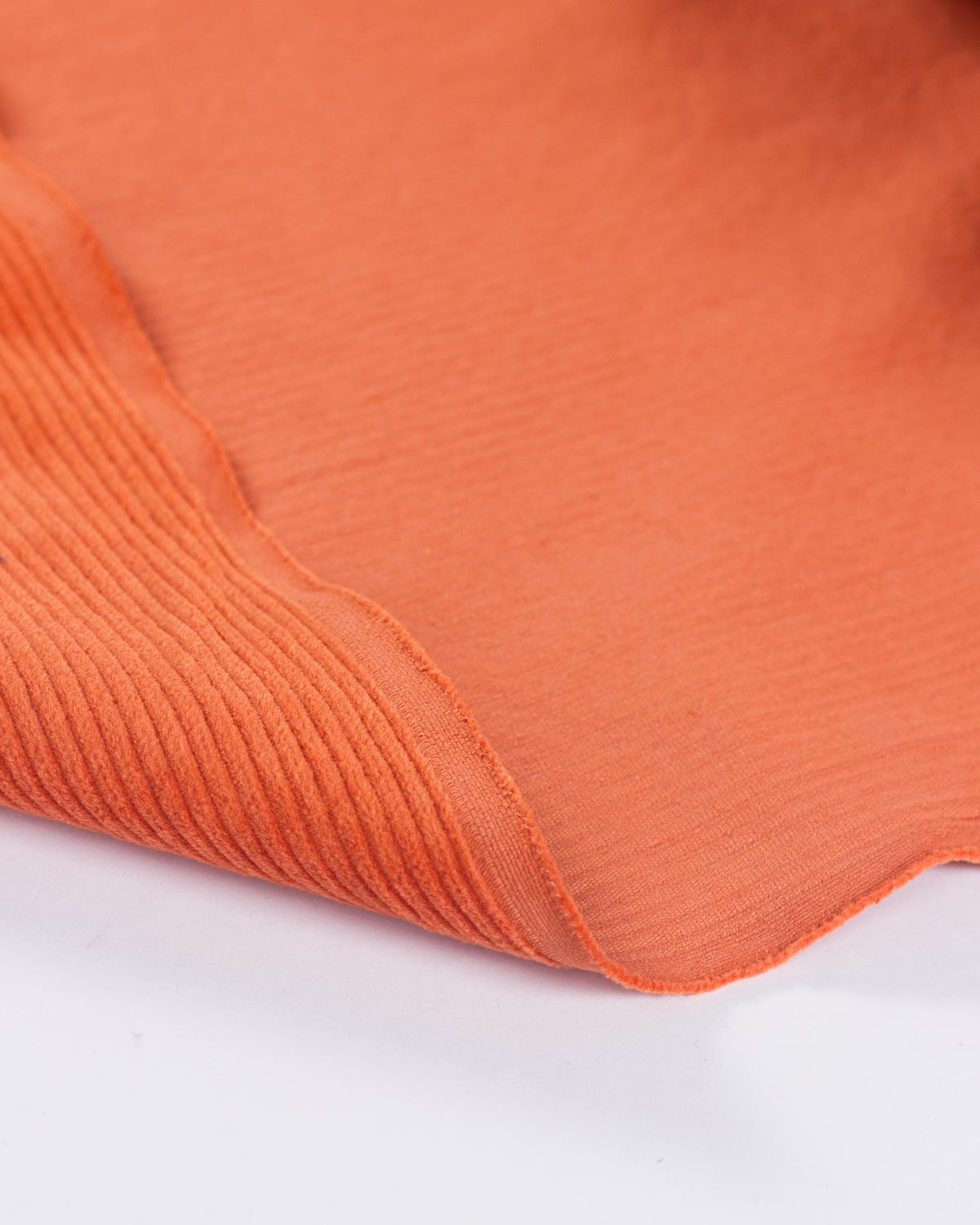 A close-up of a folded orange cotton corduroy fabric with a fine ribbed texture, showing its colour and material detail against a white background.