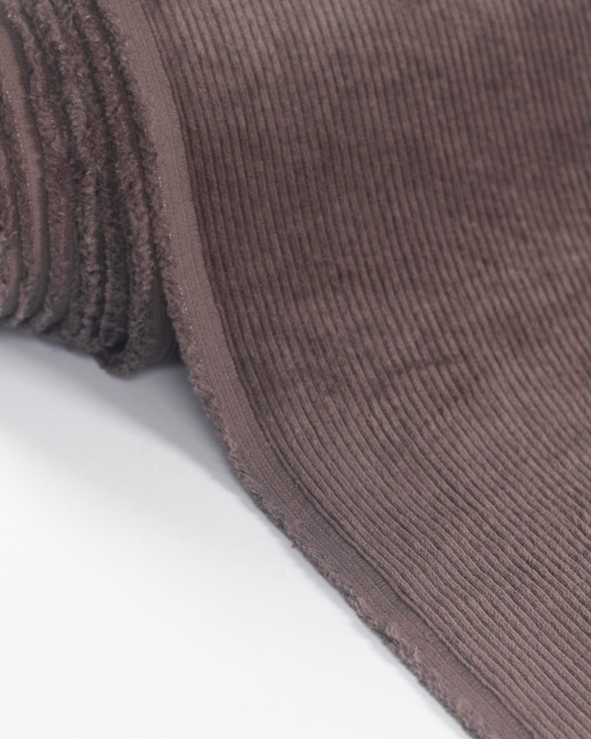 A close-up of a ribbed cotton corduroy fabric in a muted taupe-brown color, folded over to show its texture against a plain white background.