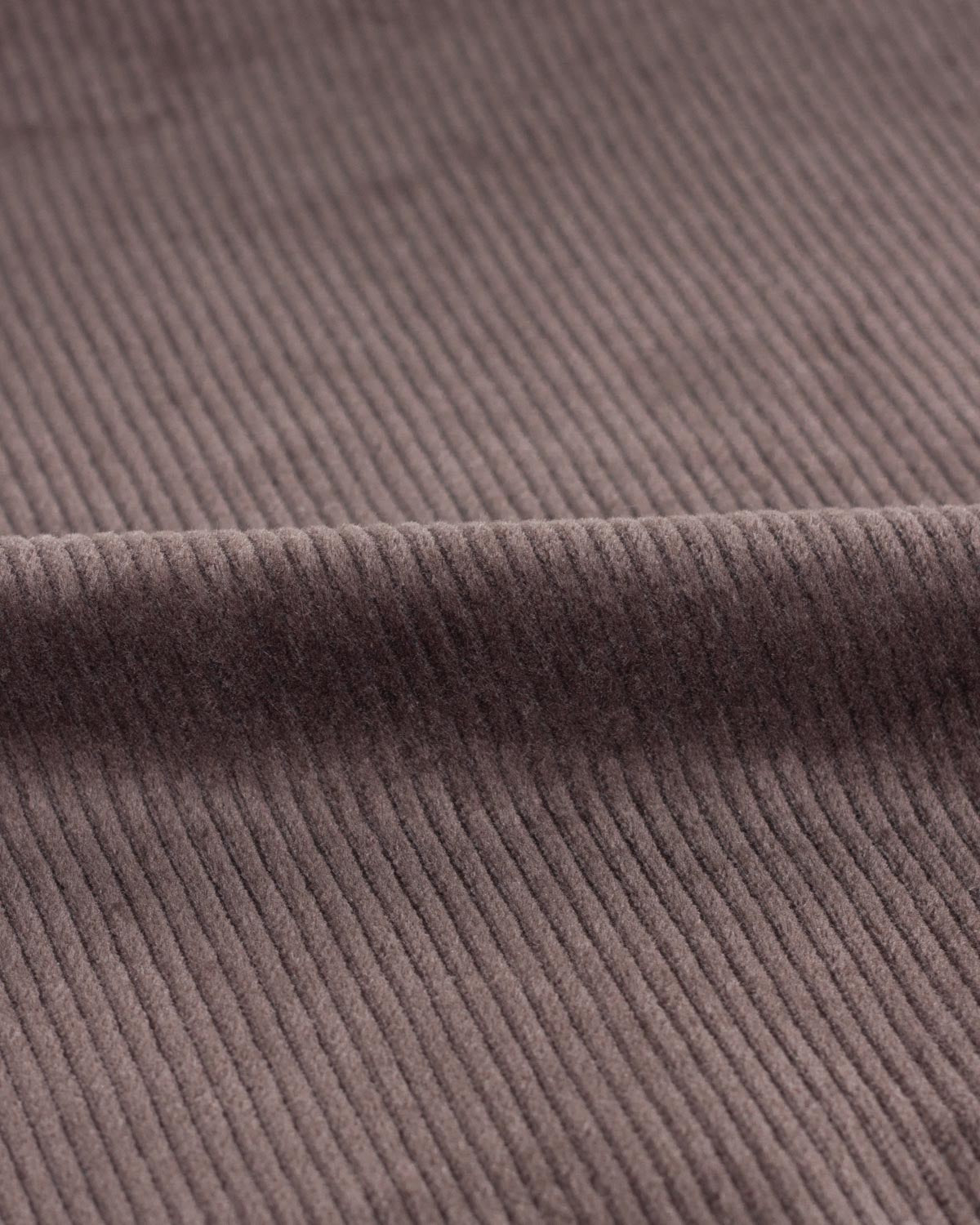 Close-up of a ribbed cotton corduroy fabric in a muted taupe-brown color, showing the texture and a fold in the material.