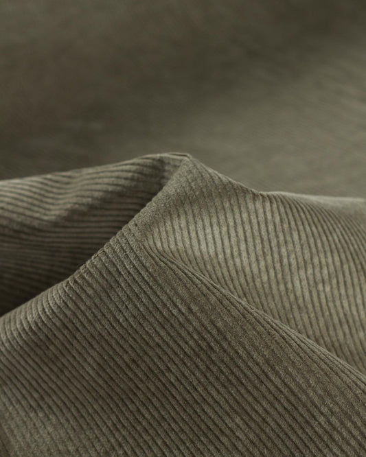 Close-up of a ribbed cotton corduroy fabric in a muted green color, showing the texture and folds.