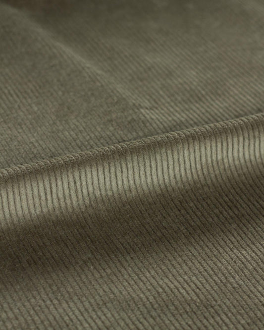 Close-up of a ribbed cotton corduroy fabric texture in a muted green color, showing soft folds.