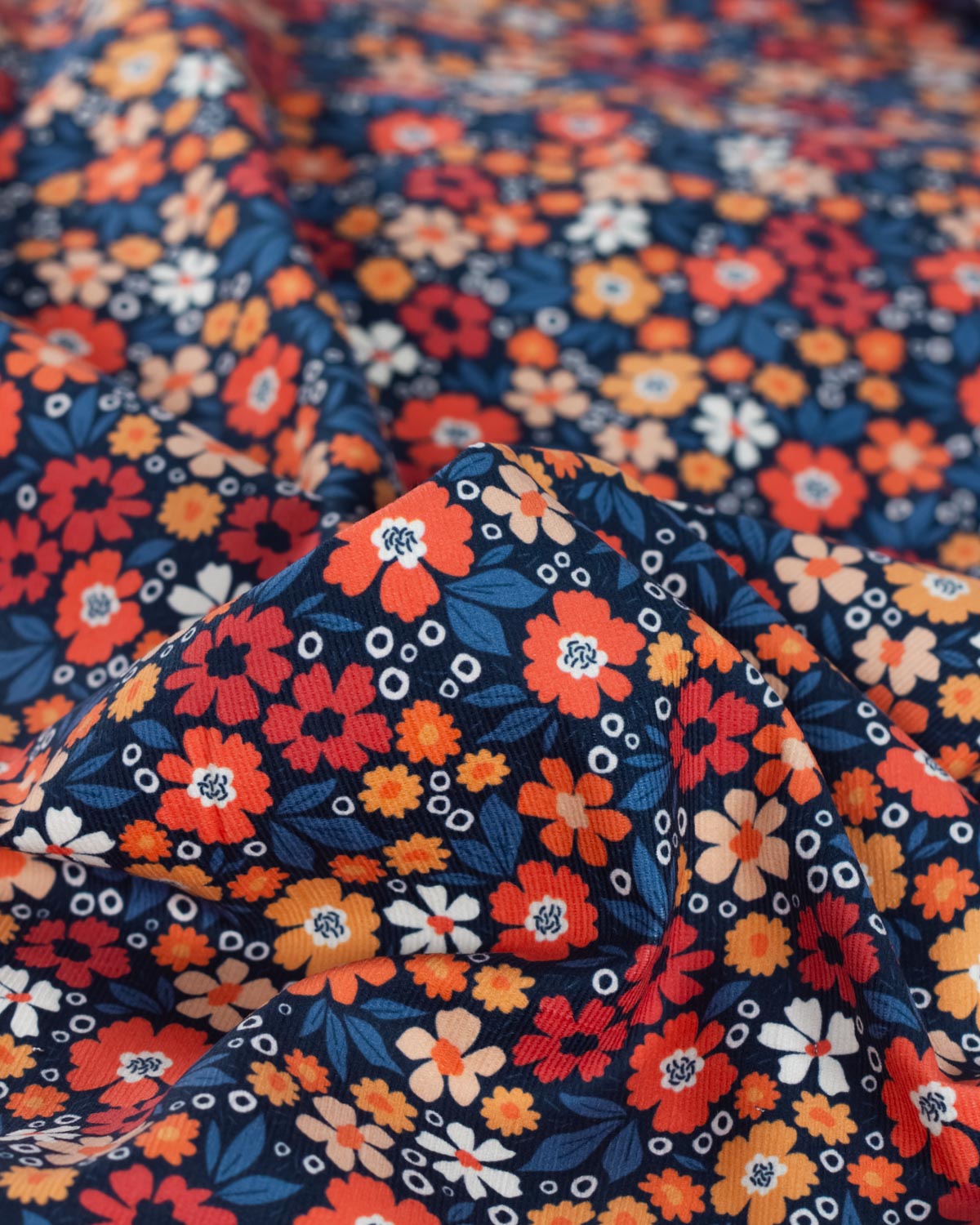 A close-up of a navy blue cotton babycord fabric with a dense, colorful floral pattern featuring orange, red, white, and light blue flowers.