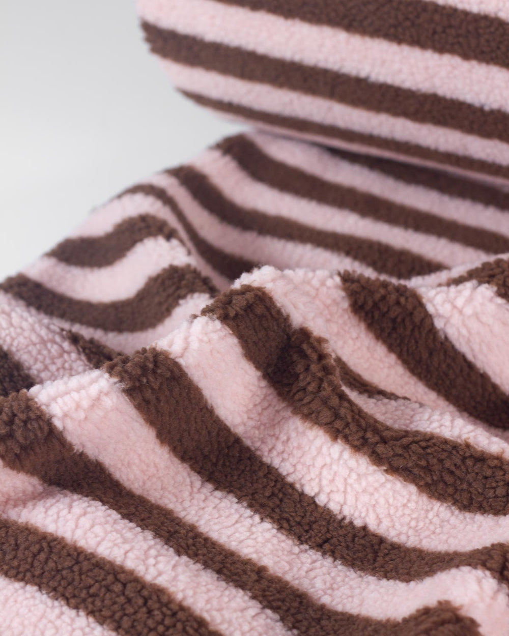 A close-up of a plush fleece fabric with alternating wavy stripes in light pink and dark brown, showing the soft textured material.