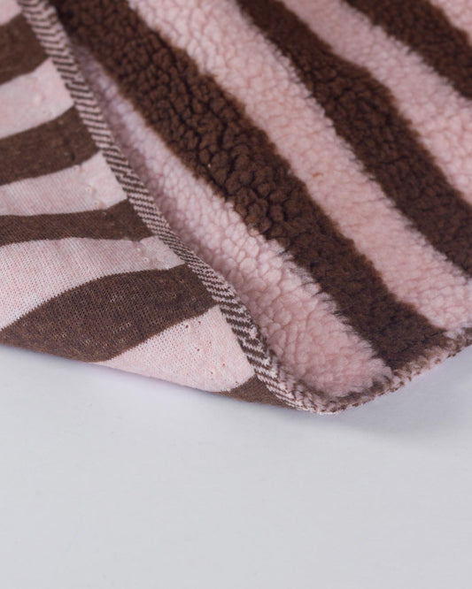 A close-up of a soft sherpa fleece fabric brown and light pink stripes, folded over to show its textured sherpa-like surface and stitched edge.