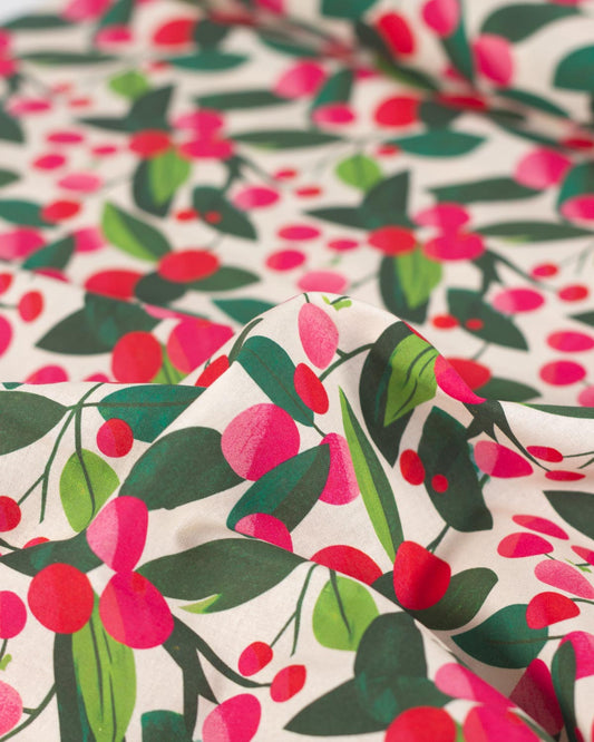 A close-up of a draped christmas cotton  fabric with a colorful botanical print featuring dark green leaves, bright pink berries, and red berries on an off-white background.