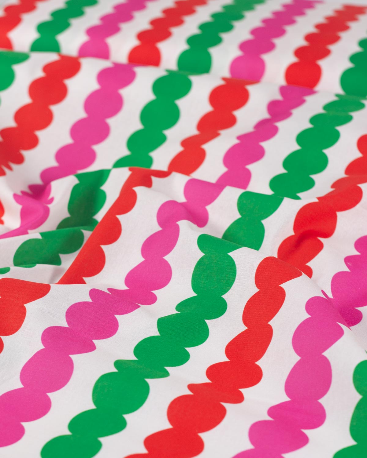 A close-up of a white cotton fabric with a repeating pattern of vertical wavy stripes in bright pink, green, and red.