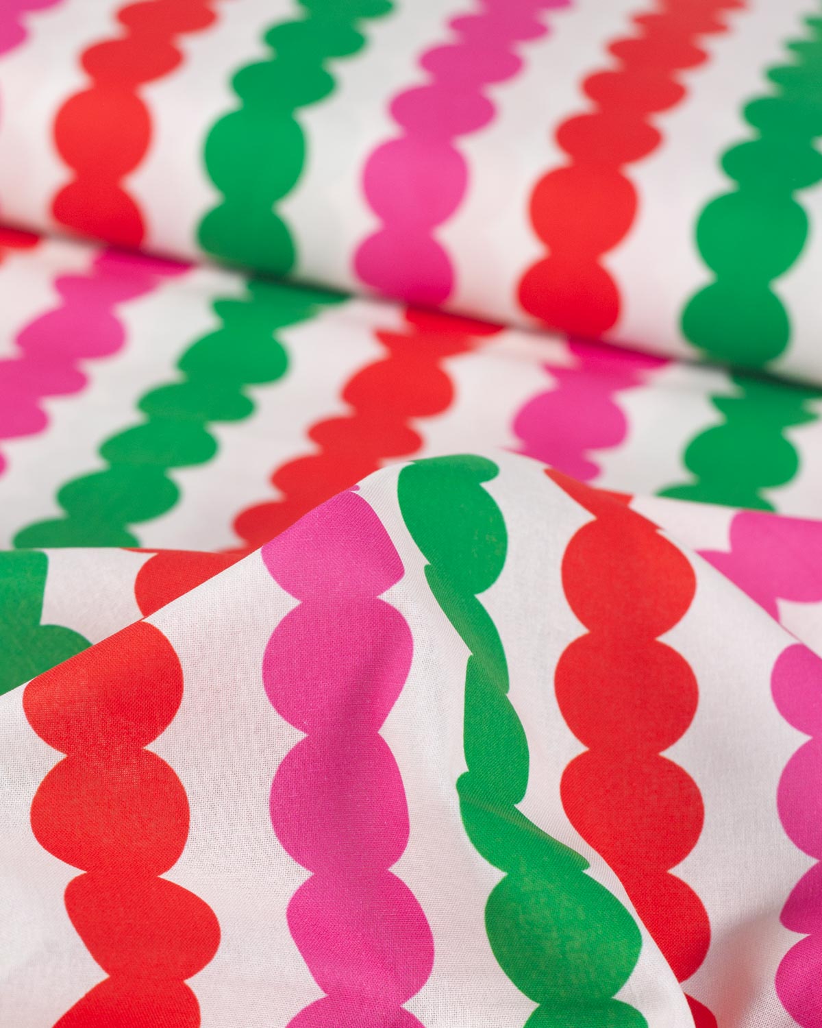 A close-up of a white fabric with a repeating vertical pattern of wavy scallop-like stripes in bright pink, green, and red.