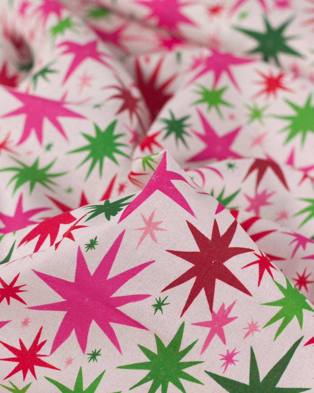 A close-up of patterned fabric with a white base and repeating starburst motifs in bright pink, red, and green.