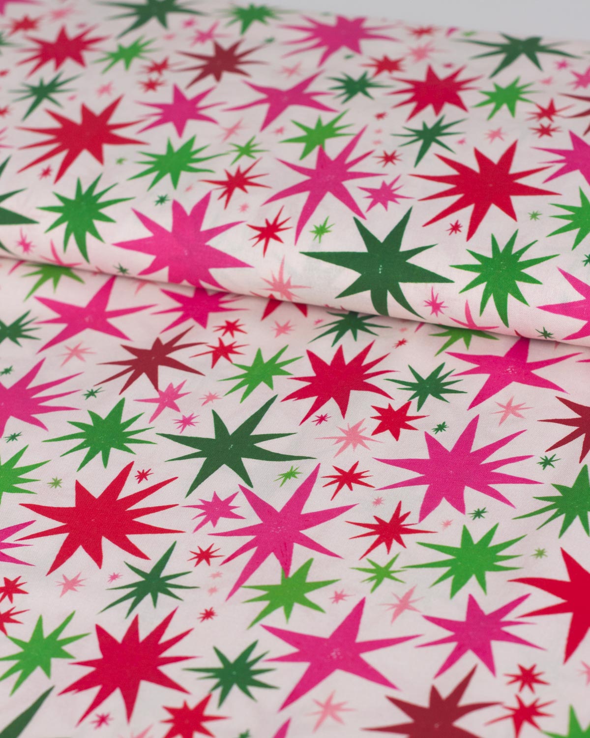 A close-up of patterned fabric with repeating starburst motifs in bright pink, green, and red on a white background.