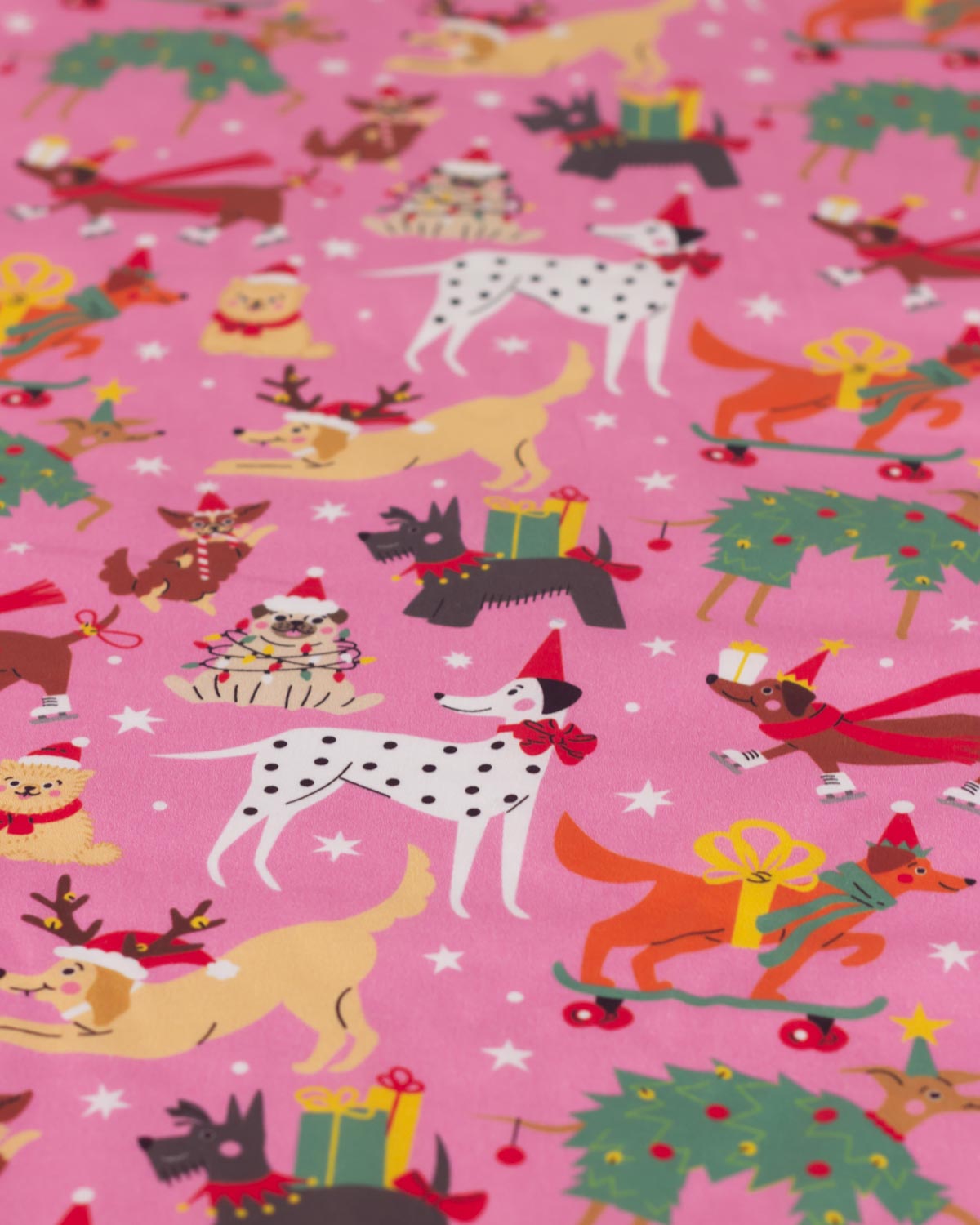 A close-up of pink Christmas-themed fabric featuring illustrated dogs, Christmas trees, gifts, and white stars in a repeating pattern.