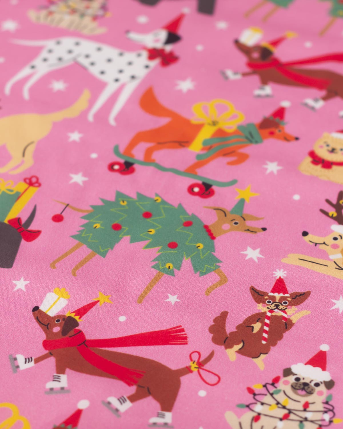A close-up of a pink fabric featuring a festive Christmas dog print with various dogs wearing Santa hats, scarves, and holiday outfits, decorated with white stars.