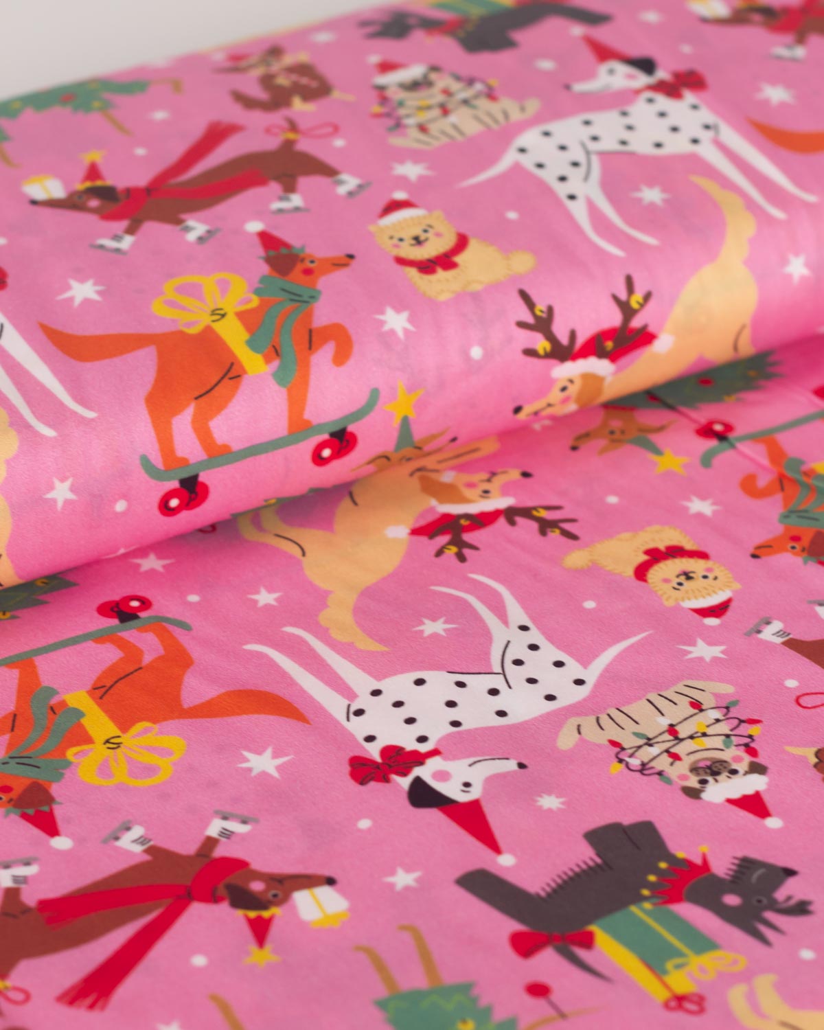 Pink Christmas cotton fabric with a festive Christmas pattern featuring cartoon dogs,  and wearing Santa hats and scarves, along with stars.