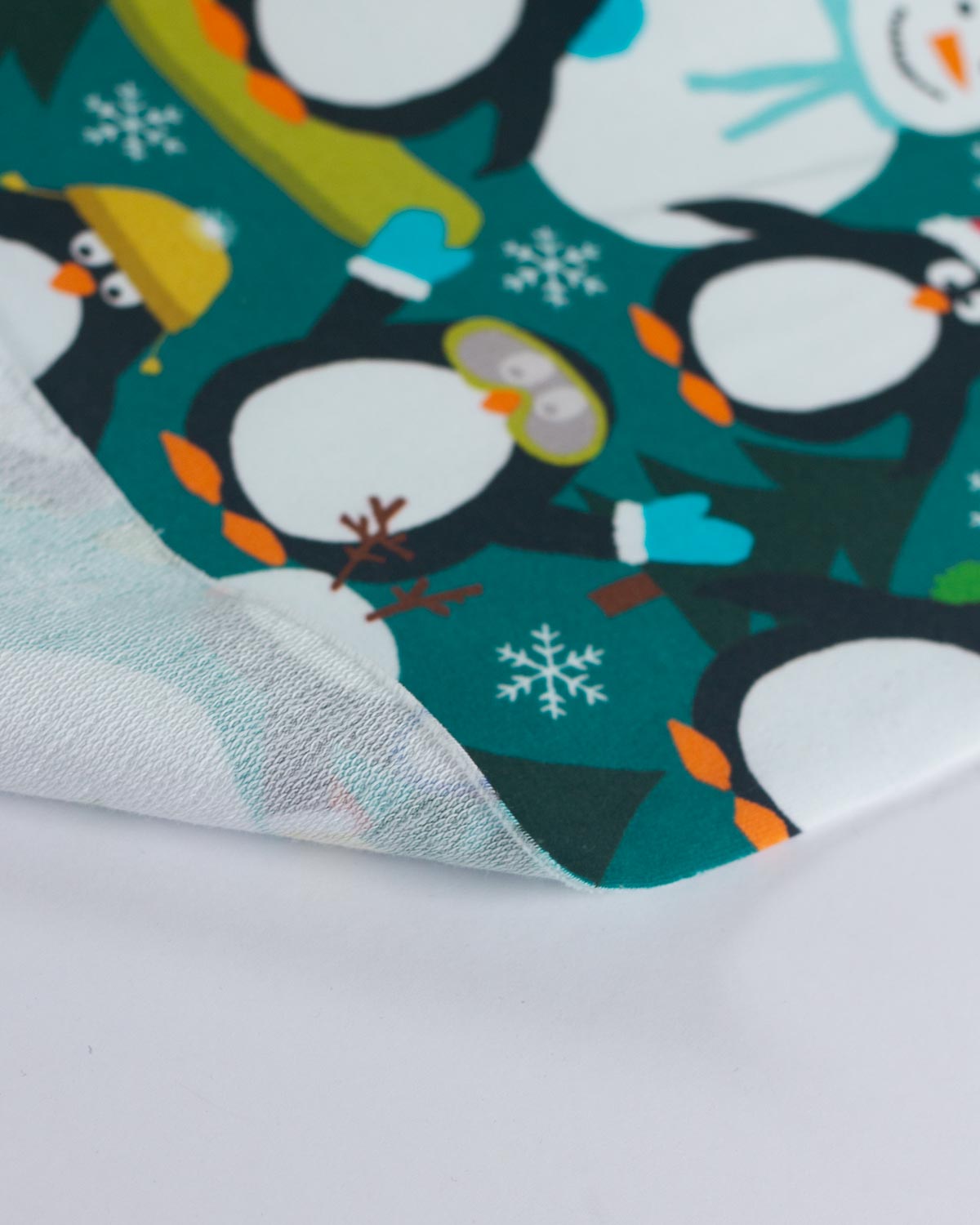 A close-up of a folded fabric featuring a penguin pattern on a teal background. The fabric is shown layered over a white surface, displaying its sheer, semi-transparent texture.