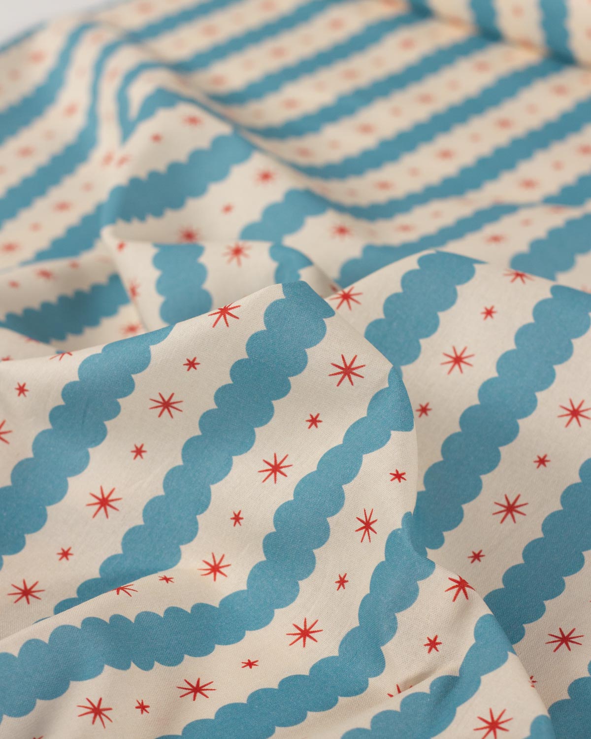 A close-up of patterned cotton fabric with alternating wavy blue and cream stripes, accented with small red starburst motifs.