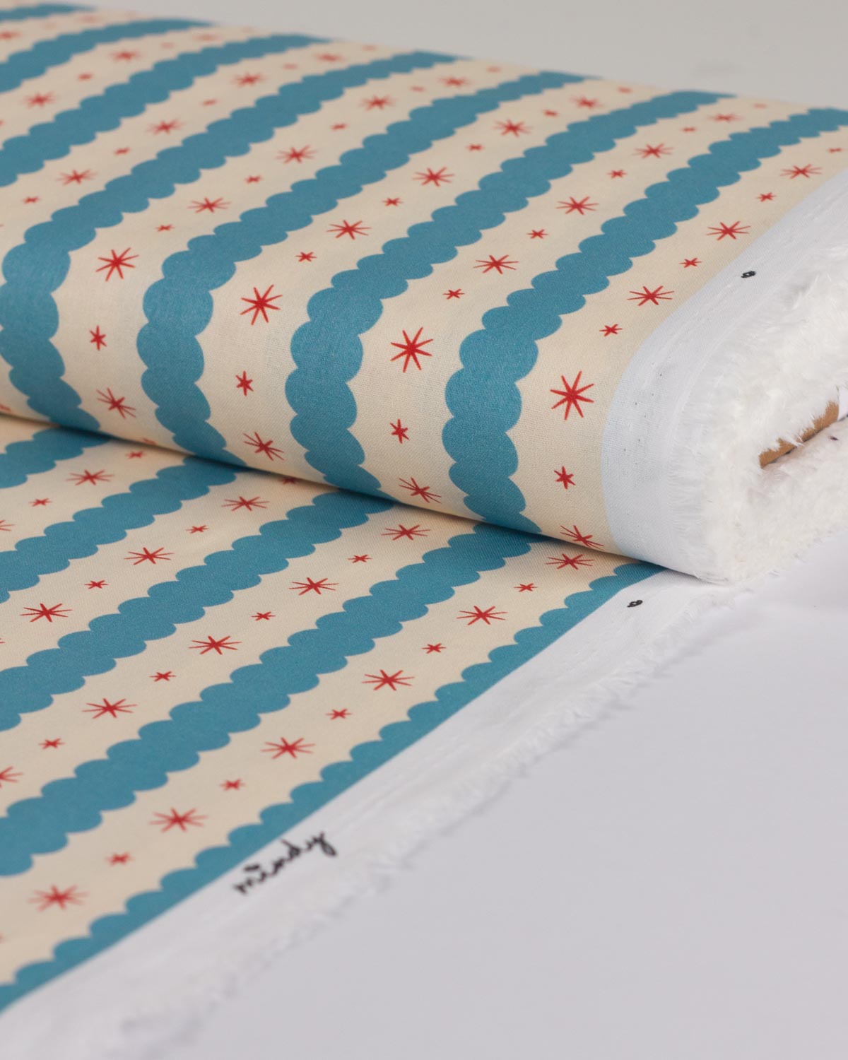 A roll of fabric with a cream background, teal blue scalloped stripes, and small red starburst motifs, shown on a white surface.