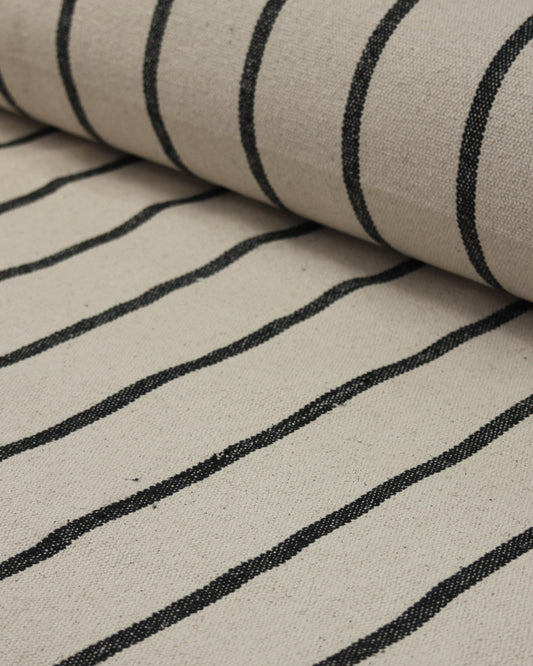 A close-up of a woven cotton upholstery fabric with a beige base and black vertical stripes