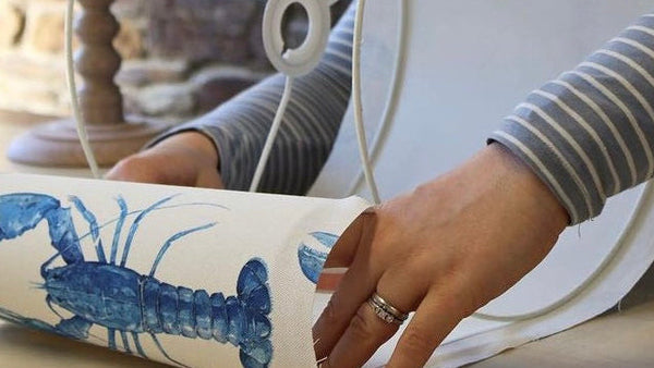 Person making a handmade lampshade with blue lobster design fabric.