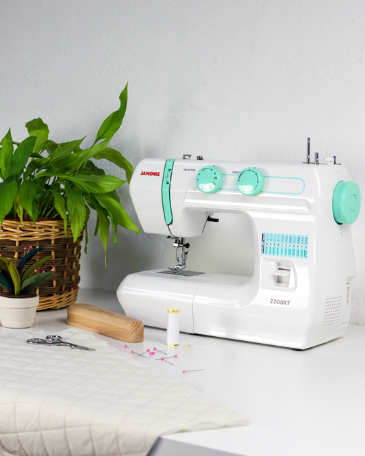 White sewing machine with green accents on a table next to a plant