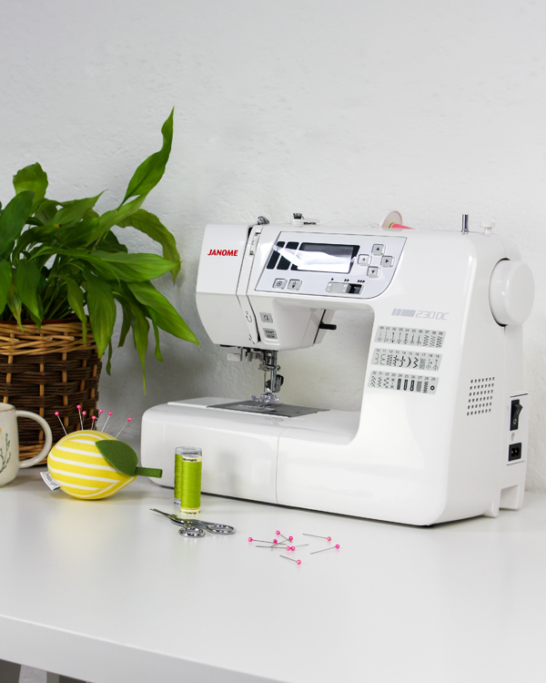 White Janome sewing machine on a white table with a plant in the background
