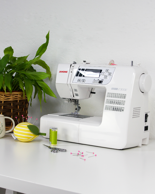 White Janome sewing machine on a white table with a plant in the background
