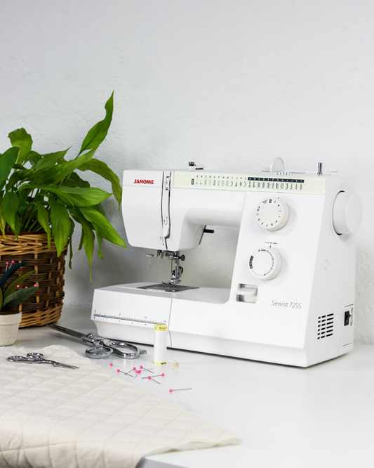 White Janome sewing machine on a white surface with a plant in the background