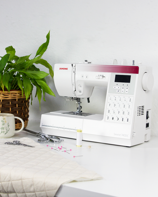White Janome 740DC sewing machine on a table with a plant and other items in the background