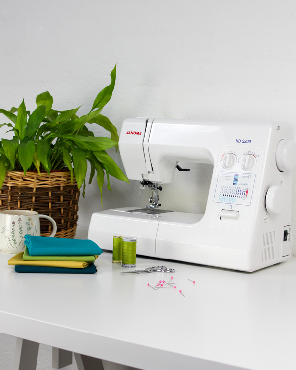 White sewing machine on a white table with a plant and fabric in the background
