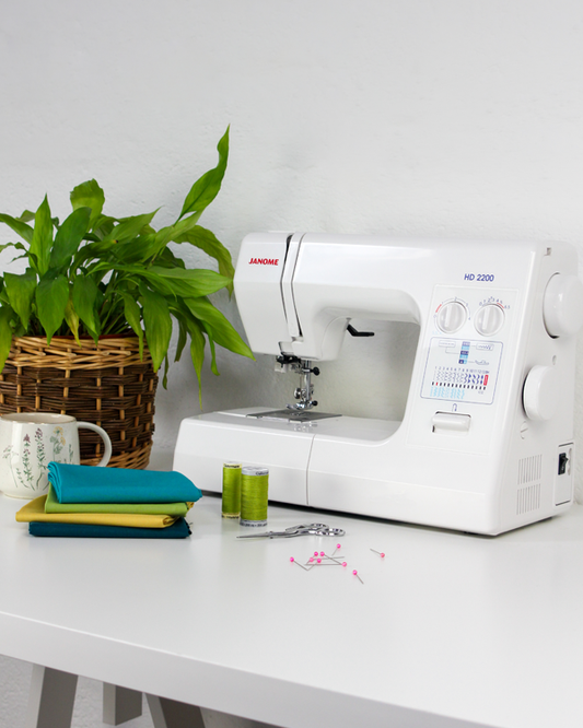 White sewing machine on a white table with a plant and fabric in the background