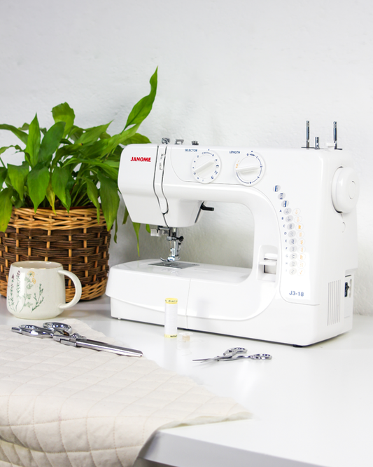 White Janome sewing machine on a table with a plant and tools in the background