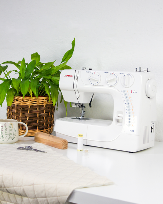 White sewing machine on a table with a plant and mug in the background