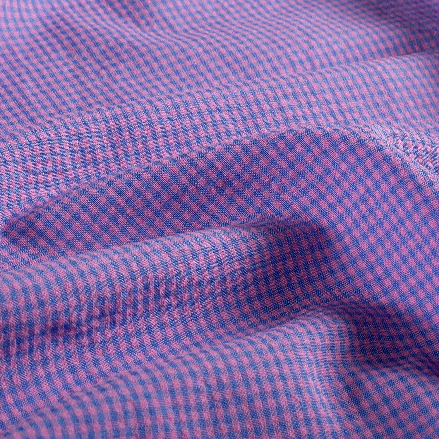 A close-up of draped fabric with a small-scale gingham check pattern in pink and blue, showing the texture and folds.